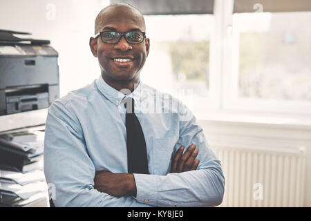 Smiling African businessman wearing a shirt and tie sitting with his arms crossed in his home office Stock Photo