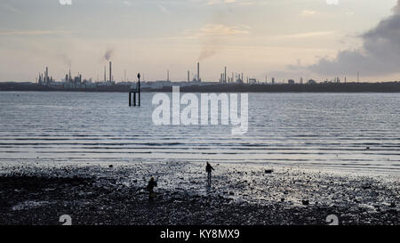 The sunset silhouettes the industrial towers of Fawley oil refinery on the shores of Southampton Water, seen from Netley. Stock Photo