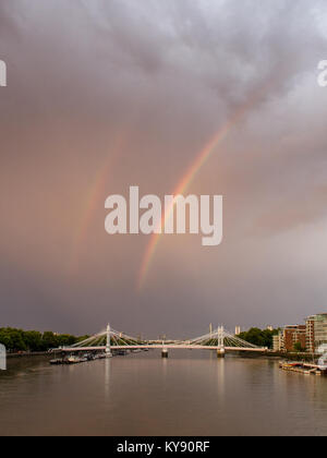 A storm passes over the River Thames and Albert Bridge at Battersea and Chelsea riversides casting a double rainbow over west London. Stock Photo