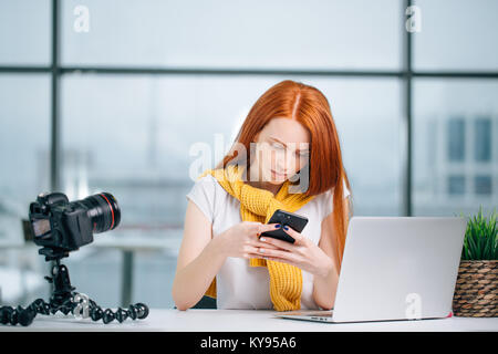 business woman sitting in office, looking at graphics and uses smartphone Stock Photo