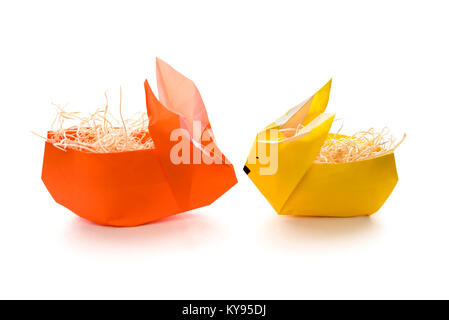 Two colorful origami bunny rabbit paper baskets in yellow and orange, stuffed with straw, ready for eggs for Easter, isolated on white background Stock Photo