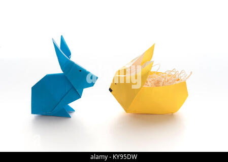 Two colorful origami bunny rabbits made of paper in yellow and blue, one stuffed with straw, ready for eggs for Easter, isolated on white background Stock Photo