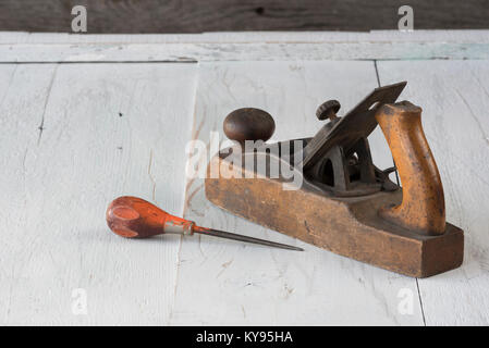 close-up of antique, vintage wooden block plane and awl with orange handle, against weathered white painted wood background Stock Photo