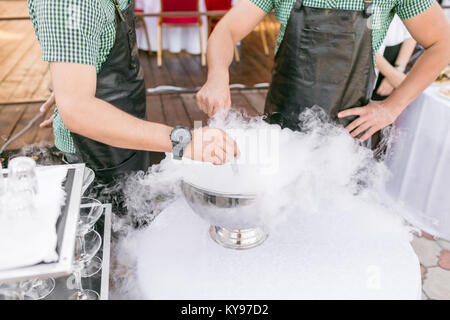 bartenders serve the cocktail in a large bowl with liquid nitrogen. row line of different alcoholic cocktails on a party. wedding day or birthday Stock Photo