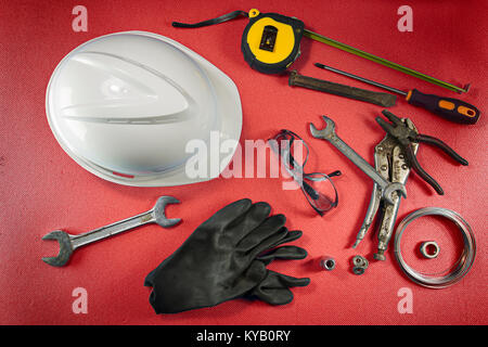 Several working tools, like a helmet, a hammer, a wrench, and other equipment, are spread on a red table. View from top. Stock Photo