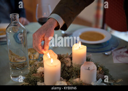 Person lighting the candles on a richly decorated Advent wreath with a match on a solemnly laid table, ready for a festive dinner at Christmas. Stock Photo