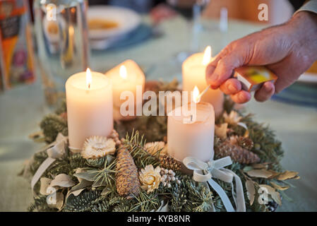 Person lighting the candles on a decorated Advent wreath with a match on a solemnly laid table, ready for a festive Christmas dinner in Austria. Stock Photo