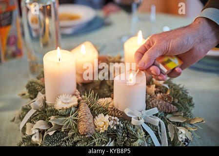 Person lighting the candles on a decorated Advent wreath with a match on a solemnly laid table, ready for a festive Christmas dinner in Austria. Stock Photo