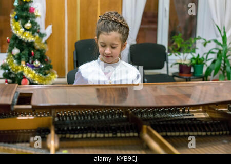 A girl in a beautiful dress plays on a brown grand piano Stock Photo