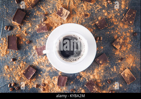 Top view cup of black coffee on a dark stone background with beans, cocoa powder and chocolate pieces scattered around. Selective focus. Space for tex Stock Photo
