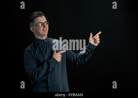 Man in glasses points with his finger to the side. Man smiling over black background Stock Photo