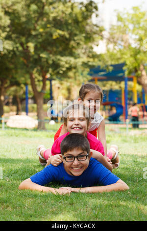 Happy children of three playing piggy back, looking at the camera. Stock Photo