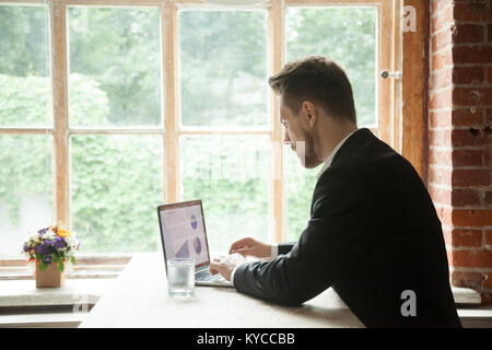 Focused serious businessman wearing suit using laptop analyzing statistics data with charts graphs on screen, concentrated manager working on project Stock Photo