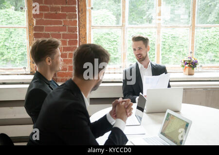 Three businessmen negotiate at meeting in boardroom, art director presenting new design project to executive male team in office, partners talking abo Stock Photo