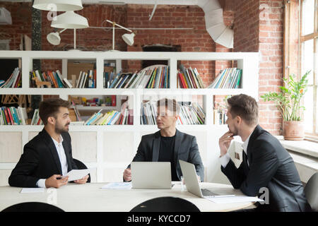 Three businessmen in suits discussing documents or project statistics sitting on executive meeting at conference office table, partners making new bus Stock Photo