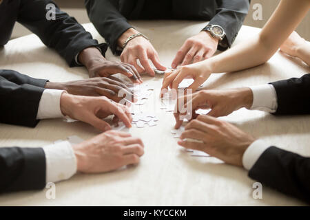 Diverse business team assembling jigsaw puzzle, hands joining pieces on desk in office, group of people playing board game, corporate common goal, hel Stock Photo