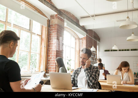 Diverse people focused on work in modern loft co-working space interior, businessman talking on phone while other businesspeople using laptops working Stock Photo