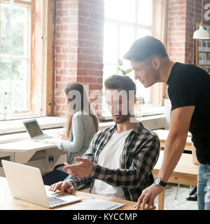 Businessman pointing at laptop screen talking to colleague discussing project in coworking space, intern asking for team leader help working together Stock Photo