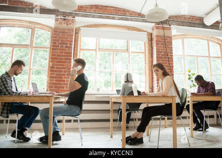 Co-working space concept, diverse people employees working in shared office together, multiracial business men and women sitting at desks using device Stock Photo