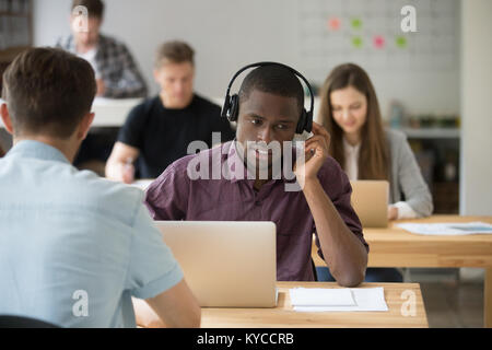 African american sales manager wearing wireless headset consulting client at support co-working office desk, black call center agent in headphones tal Stock Photo