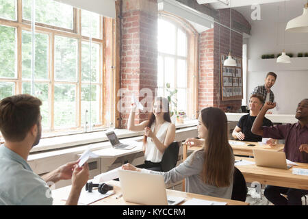 Multiracial corporate team launching paper planes in coworking office interior, diverse employees group laughing having fun at work, lazy workers wast Stock Photo