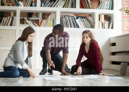 Young multi-ethnic project team brainstorming on office floor, african american leader teaching female managers or designers working together discussi Stock Photo