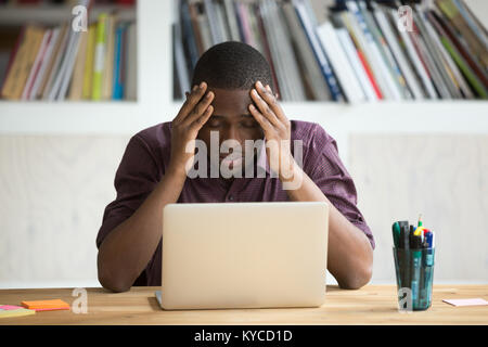 Frustrated black man feeling depressed after fail, upset african-american businessman sitting in front of laptop stressed about bankruptcy debt, dark- Stock Photo