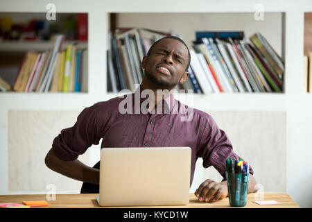 African-american man touching back sitting at desk feeling sudden backache, black businessman suffering from low-back lumbar pain after sedentary work Stock Photo
