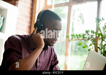 African american man enjoying good music in headphones with eyes closed, young black casual guy listening to favorite mp3 digital music on laptop wear Stock Photo