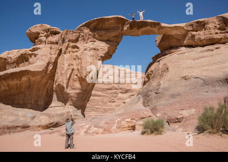 Tourists next to a Burdah bridge rock formation in the desert of Wadi Rum, Jordan Stock Photo