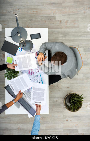 Directly above view of busy dark-haired entrepreneur sitting at office desk while his colleagues passing him several contracts for signature Stock Photo
