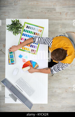 Talented young fashion designer sitting at desk of modern studio and choosing fabric colors for his new collection, directly above view Stock Photo