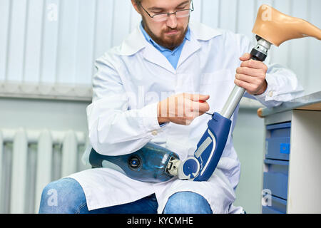 Portrait of bearded technician checking artificial limb while sitting at desk in office, adjusting it and checking for quality Stock Photo