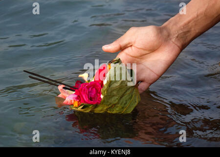 A woman's hand floating a holy package of flowers and agarbatti in hindu holy river ganga at ghat in rishikesh, India Stock Photo