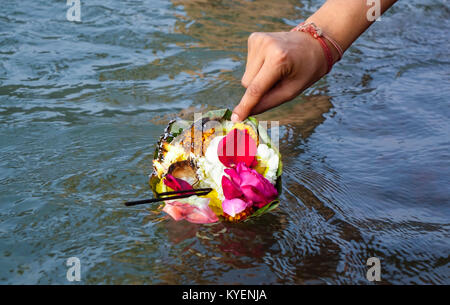 A woman's hand floating a holy package of flowers and agarbatti in hindu holy river ganga at ghat in rishikesh, India Stock Photo