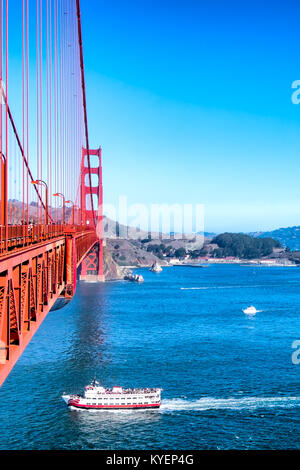 San Francisco ferry boat going under the Golden Gate Bridge. Aerial view from the bridge deck. Bright blue sky and water. Copy space. Vertical Stock Photo