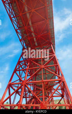 Golden Gate Bridge viewed from underneath, looking up at the orange girder structure. Blue sky in the background. Unusual view of the iconic landmark. Stock Photo