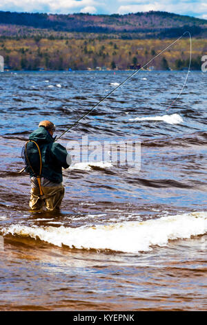 man wearing waders and fishing clothes examines edge of lakebed for flies  before going flyfishing Stock Photo - Alamy