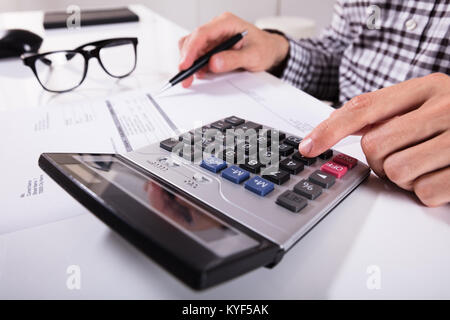 Close-up Of Businessman's Hands Calculating Invoice Using Calculator With Eyeglasses On Desk Stock Photo