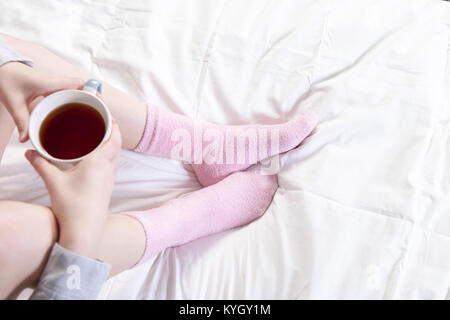 Hands holding a cup of coffee. You can see the legs in pink socks. Stock Photo