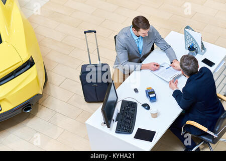 Above view of handsome man reading lease contract sitting at desk in dealership shop before renting luxury car for business travelling, copy space Stock Photo