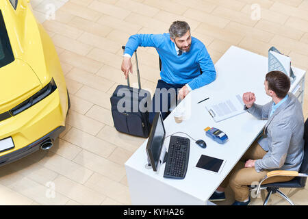 Above view of mature man talking to car salesman sitting at desk in dealership shop before renting luxury car for travelling, copy space Stock Photo