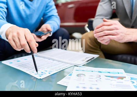 Close up of two unrecognizable young men discussing sales strategies and marketing statistics sitting at coffee table with charts and graphs Stock Photo