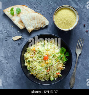 Tabbouleh salad and flatbread on concrete background. Lebanese, arabic cuisine. Healthy vegan cous cous salad in black bowl. Table top view, square cr Stock Photo