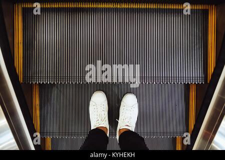 Selfie of  man feet in white sneaker shoes on escalator steps in the shopping mall, top view in vintage style Stock Photo