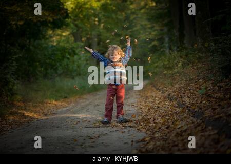Young blonde boy with long curly hair playing in outdoor in autumnal forest. Stock Photo