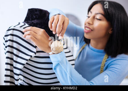 Professional young tailor taking a pin from a pin cushion while working Stock Photo