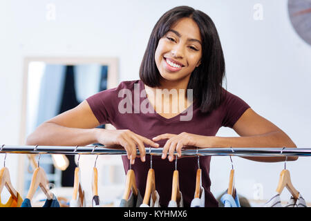 Delighted woman smiling while leaning on a clothes rail Stock Photo