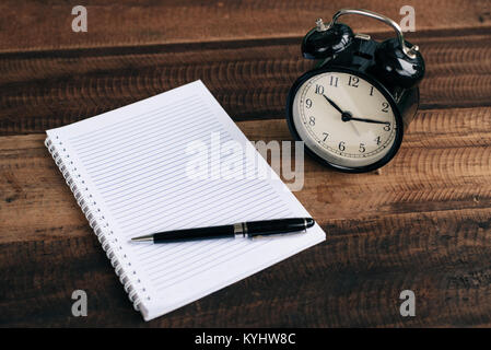 clock, pen and blank notebook on wooden table background Stock Photo