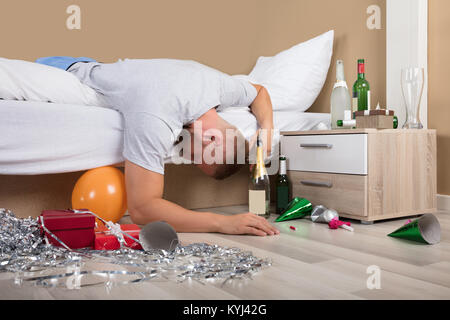 Young Man Lying On Bed With Messed Up Floor After Party Stock Photo